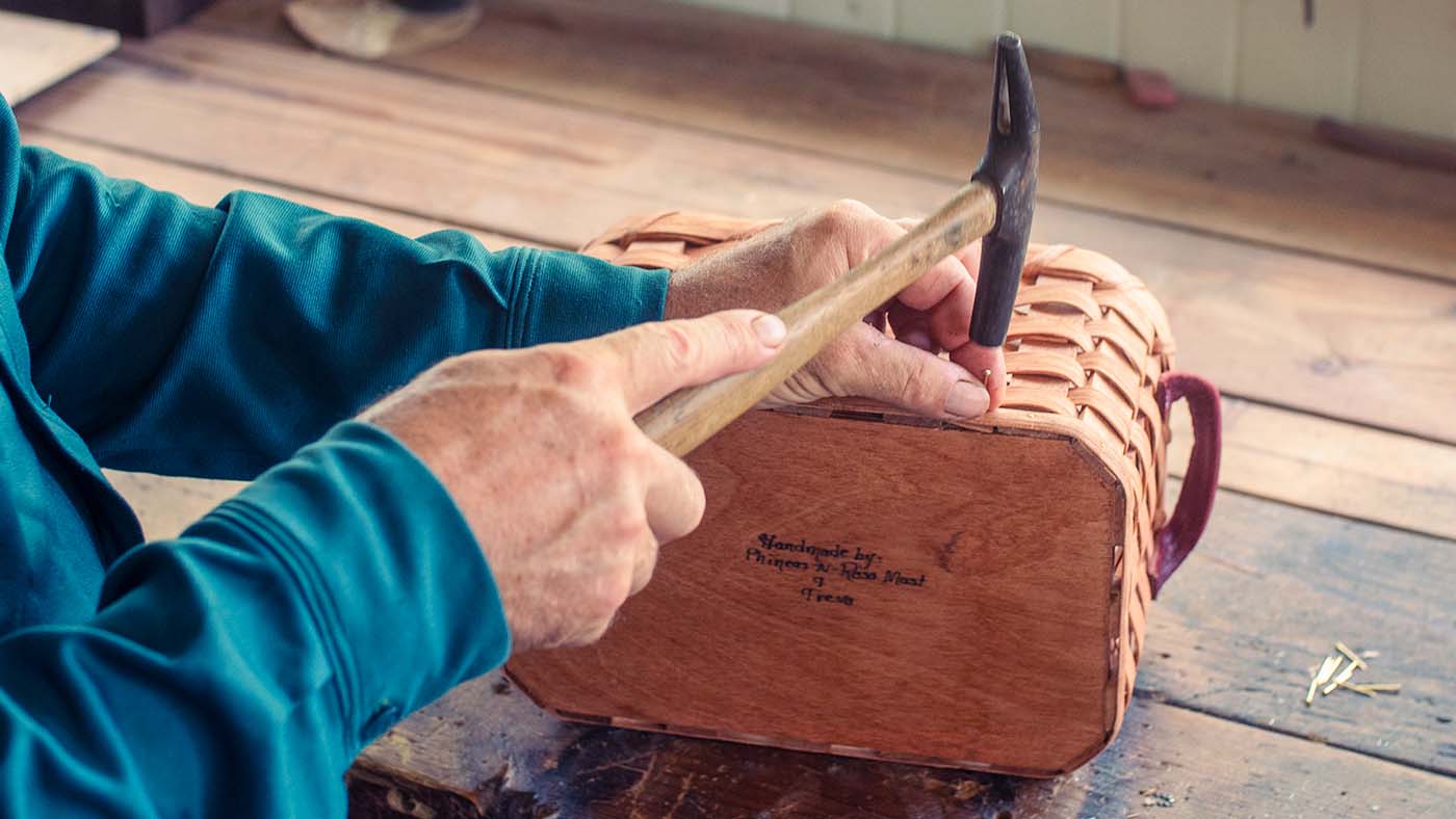 Amish craftsman nailing the solid wood bottom onto a handwoven basket